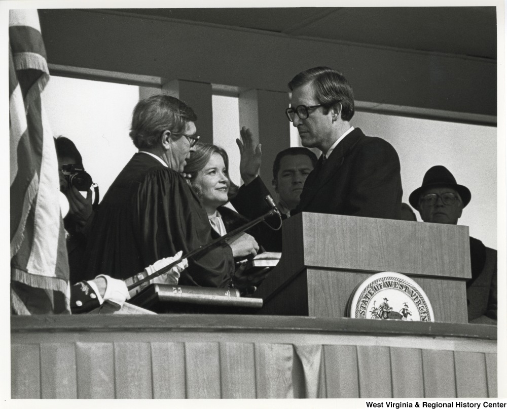 ["Governor Jay Rockefeller taking the oath of office  for the second time by the Honorable Sam R. Harshbarger, Chief justice of the Supreme Court of Appeals of West Virginia, as Sharon Rockefeller looks on."]%